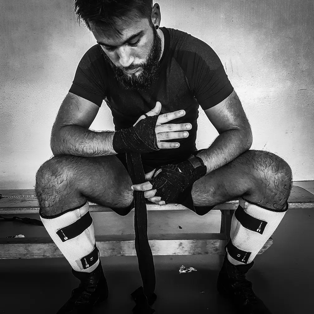 Boxeur assis en train d’enrouler ses bandes de protection avant une séance de boxe pieds-poings.