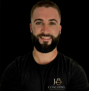 Portrait d’un coach sportif souriant, photographié sur fond noir.