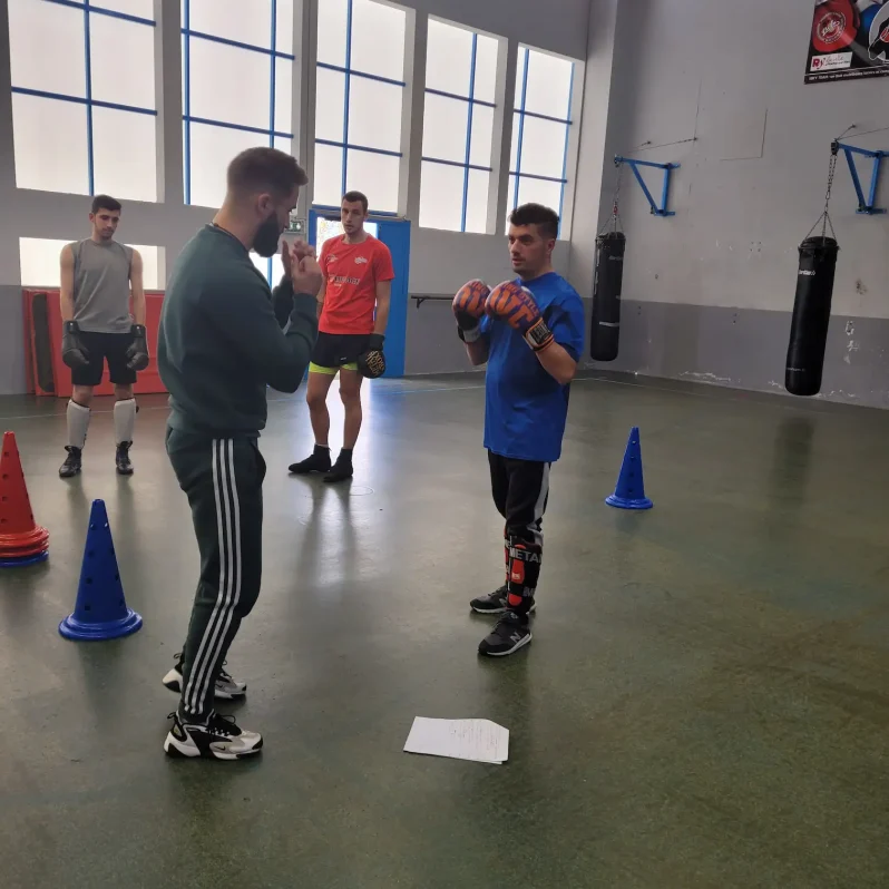 Coach donnant des consignes techniques à un groupe d’élèves en posture de garde lors d’un cours de cardio boxing en salle.