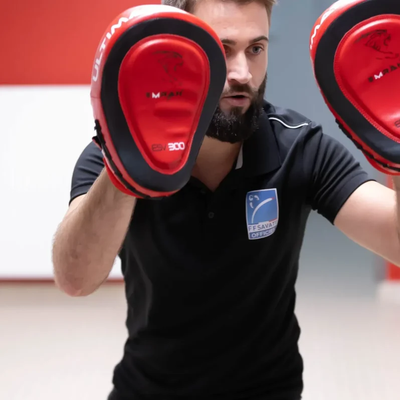 Coach tenant des pattes d’ours face à une élève lors d’un entraînement de cardio boxing.