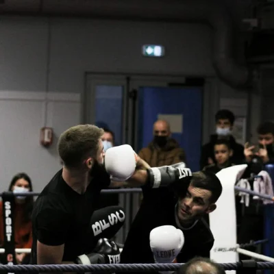 Combat de boxe pieds-poings sur un ring avec deux pratiquants échangeant des coups, sous les yeux du public.
